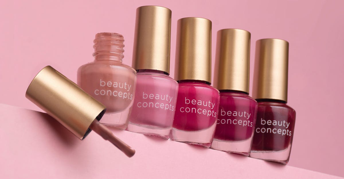 Five nail polish bottles lined up with one open on a pink background.