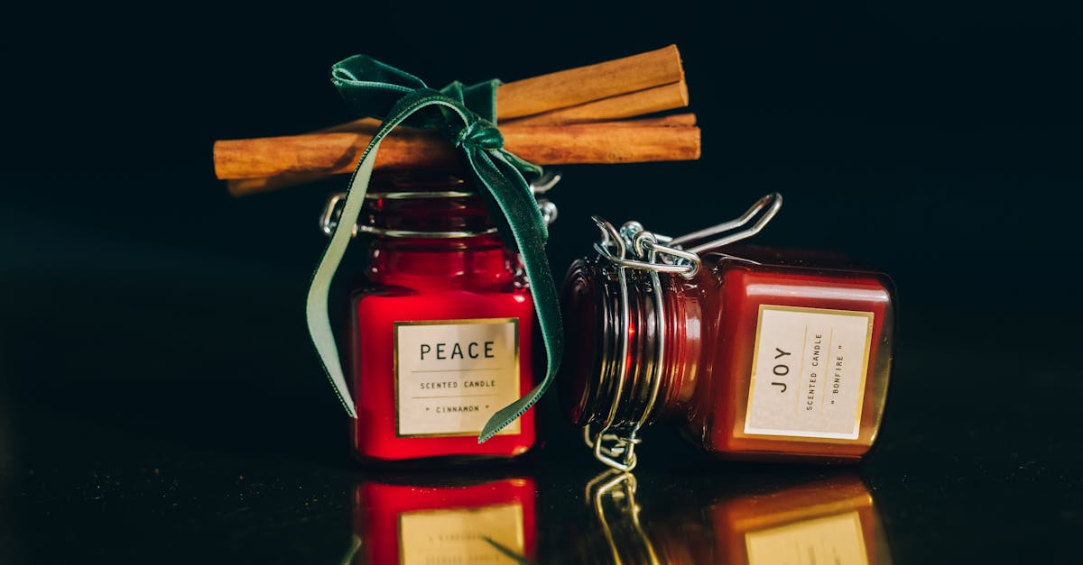 Glass jar scented candles with cinnamon sticks on a reflective surface, perfect for cozy atmospheres.