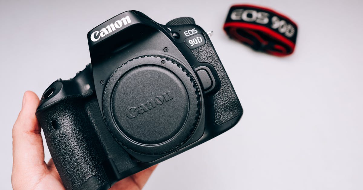 Close-up of a DSLR camera held by a hand against a plain background.